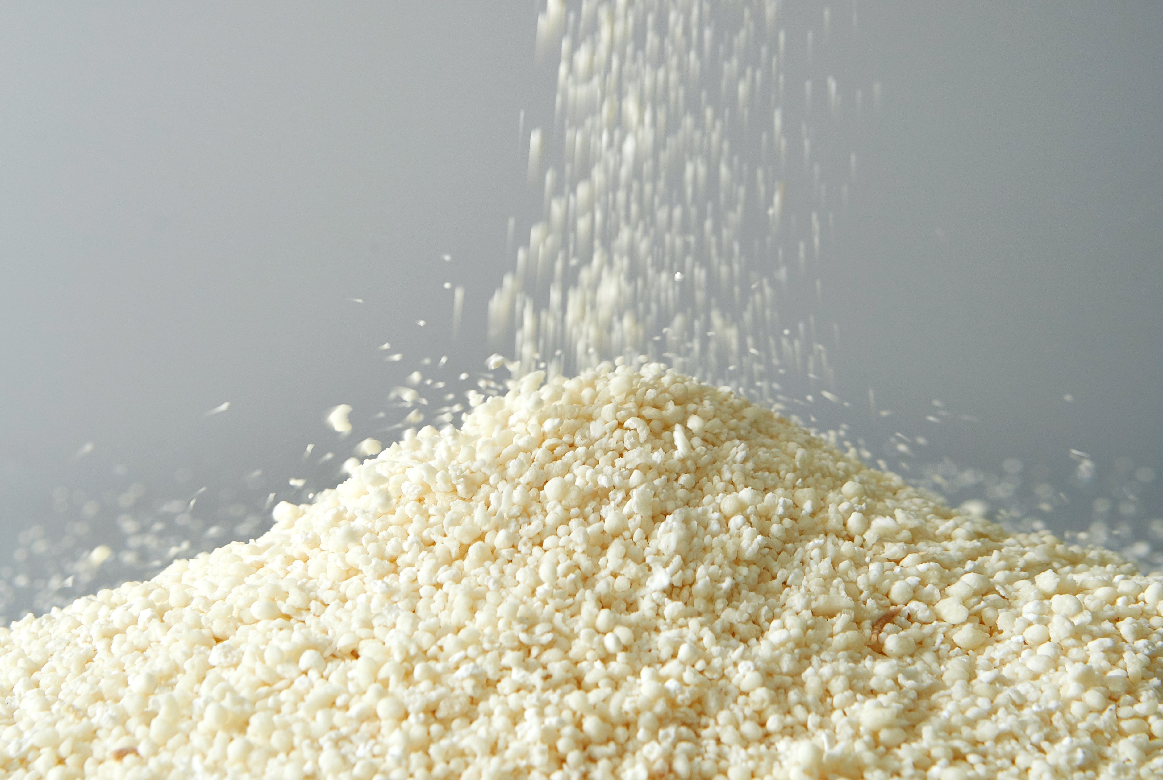 White granulated substance being poured onto a pile on a gray background